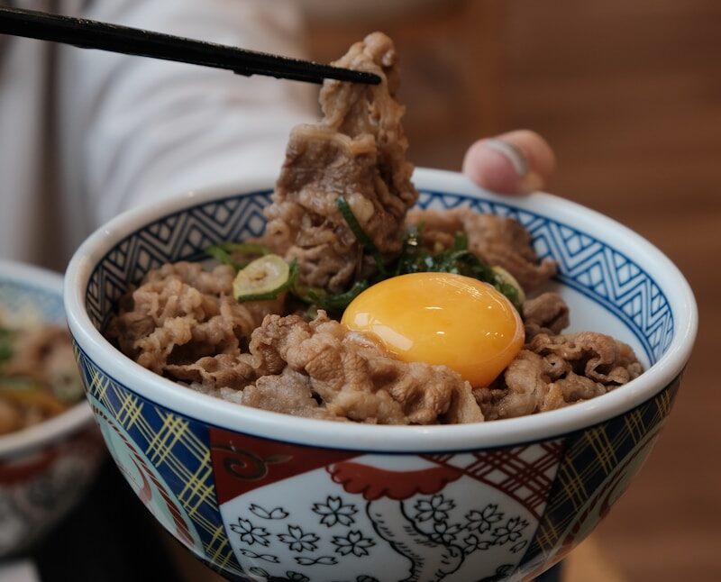 Bowl of beef and rice topped with raw egg.